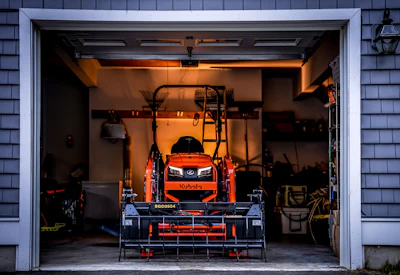 Orange compact tractor with front-end loader mounted on service lift in organized garage workshop