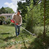 Man using a red string trimmer to edge grass along a fence in a residential yard