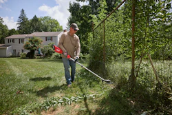 Man using a red string trimmer to edge grass along a fence in a residential yard