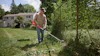 Man using a red string trimmer to edge grass along a fence in a residential yard