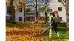 Worker in safety gear using leaf blower to clear fallen autumn leaves from residential yard