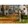 Worker in safety gear using leaf blower to clear fallen autumn leaves from residential yard