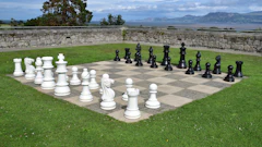 Outdoor giant chess game with white and black pieces on stone board in scenic lakeside garden setting