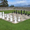 Outdoor giant chess game with white and black pieces on stone board in scenic lakeside garden setting