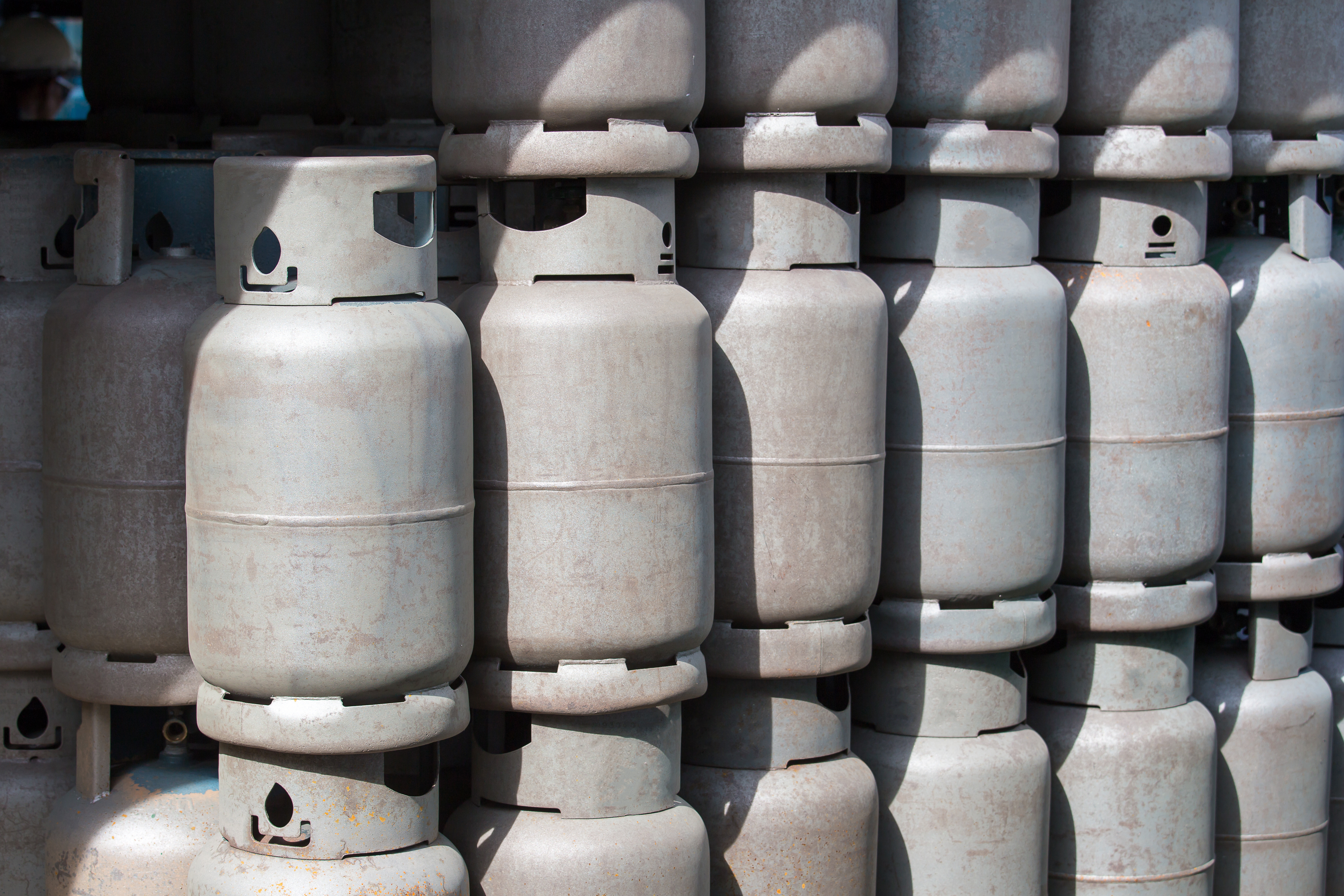 Multiple white propane cylinders stacked in rows with valve caps visible on top