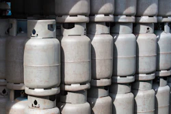 Multiple white propane cylinders stacked in rows with valve caps visible on top