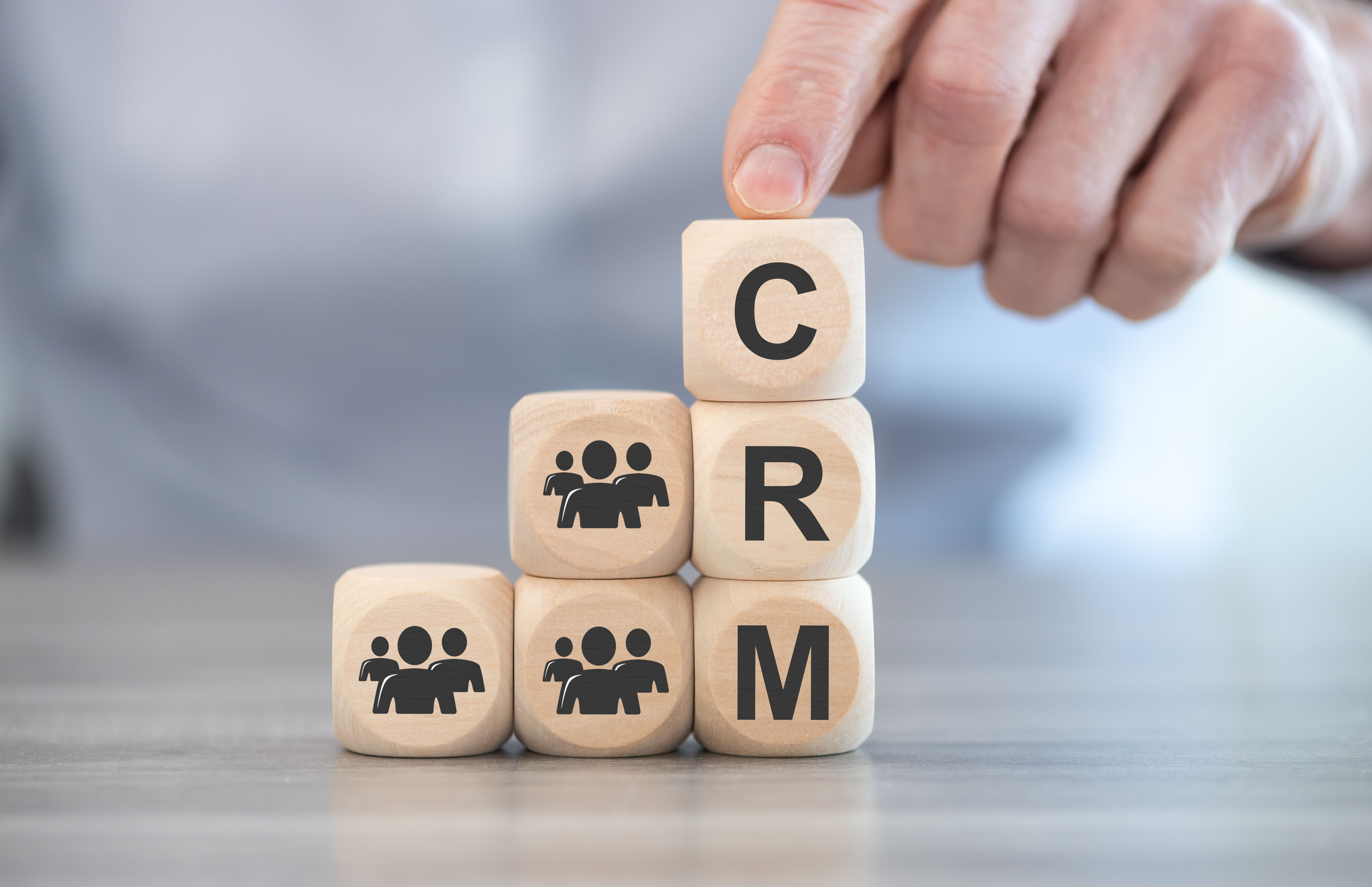 Hand placing wooden block with letter C on stacked blocks spelling CRM with people icons