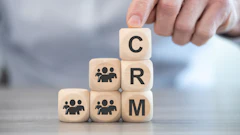 Hand placing wooden block with letter C on stacked blocks spelling CRM with people icons