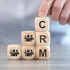 Hand placing wooden block with letter C on stacked blocks spelling CRM with people icons