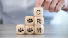 Hand placing wooden block with letter C on stacked blocks spelling CRM with people icons
