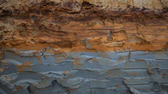 Stratified rock formation showing layered sedimentary deposits with rust-colored oxidation and weathered surfaces