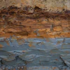 Stratified rock formation showing layered sedimentary deposits with rust-colored oxidation and weathered surfaces