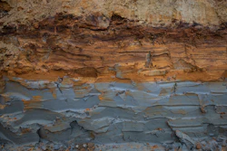 Stratified rock formation showing layered sedimentary deposits with rust-colored oxidation and weathered surfaces