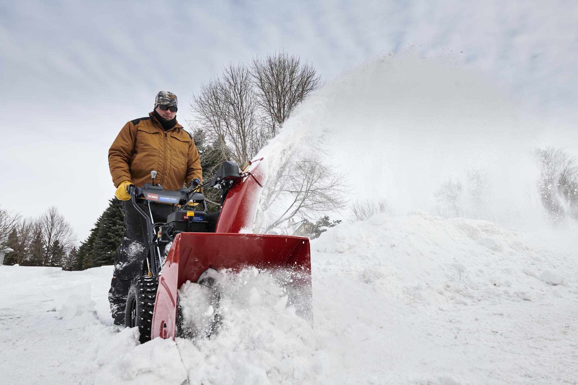Person operating a red snow blower clearing snow from a driveway in winter