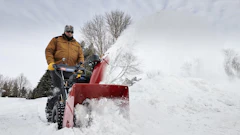 Person operating a red snow blower clearing snow from a driveway in winter