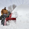 Person operating a red snow blower clearing snow from a driveway in winter