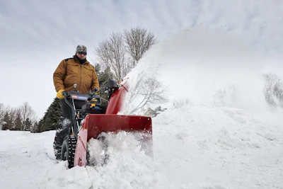 Person operating a red snow blower clearing snow from a driveway in winter