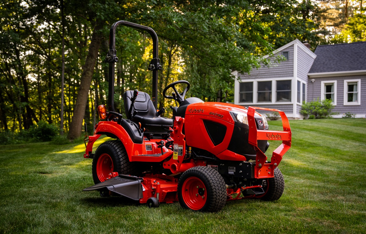 Red zero-turn radius riding mower on manicured lawn with residential house and trees in background