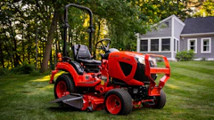 Red zero-turn radius riding mower on manicured lawn with residential house and trees in background