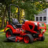 Red zero-turn radius riding mower on manicured lawn with residential house and trees in background