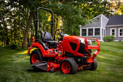 Red zero-turn radius riding mower on manicured lawn with residential house and trees in background