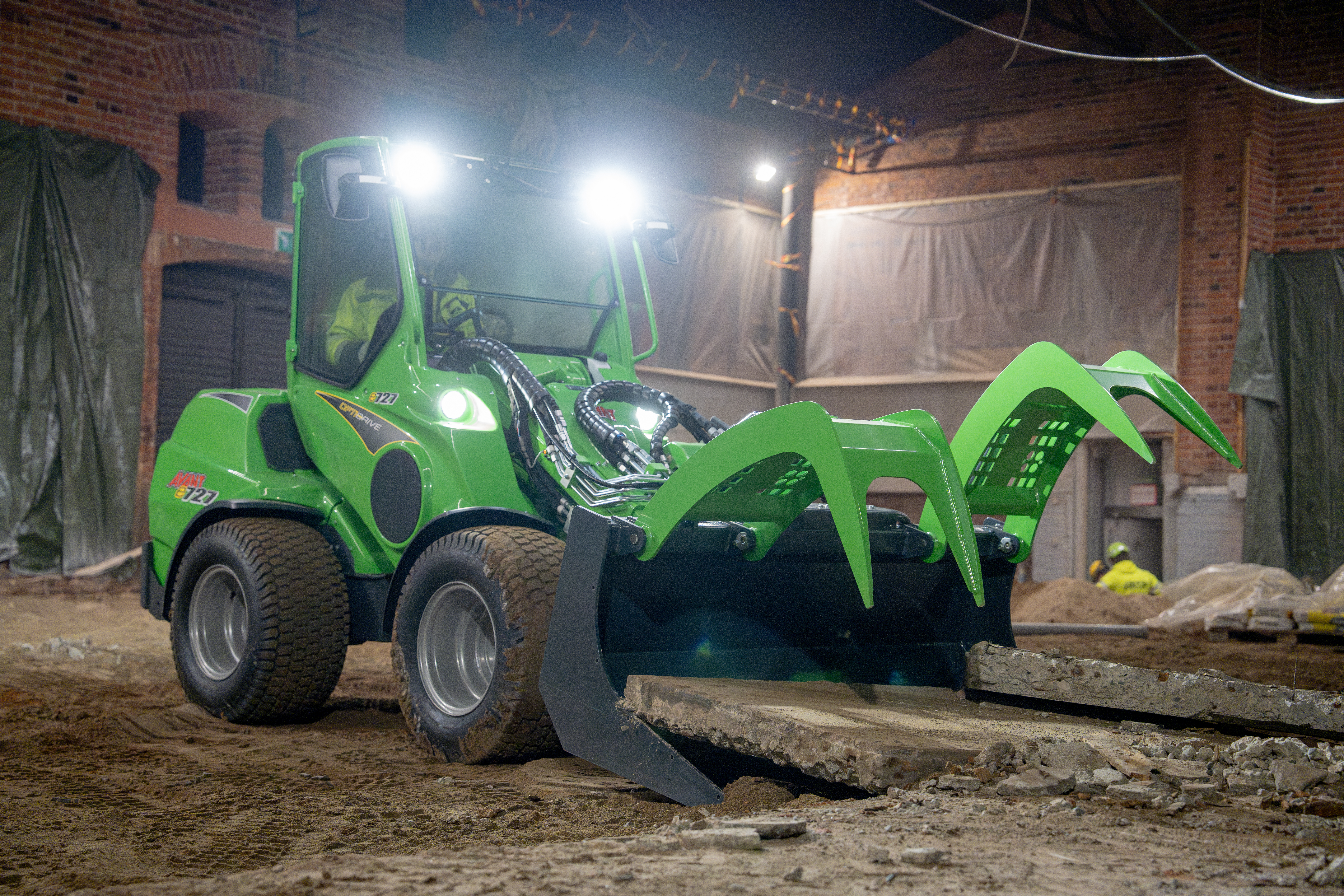 Bright green wheeled loader with articulated bucket attachment on construction site at night