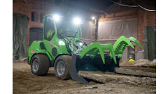 Bright green wheeled loader with articulated bucket attachment on construction site at night