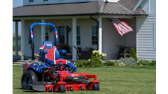 Patriotic red and blue zero-turn radius mower on residential lawn with American flag and house in background
