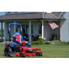 Patriotic red and blue zero-turn radius mower on residential lawn with American flag and house in background