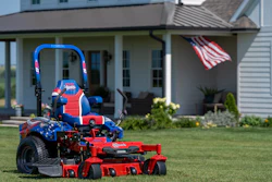 Patriotic red and blue zero-turn radius mower on residential lawn with American flag and house in background