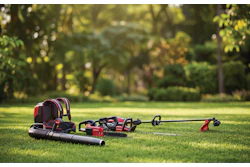 Red and black power tools and equipment laid out on grass with green trees in background