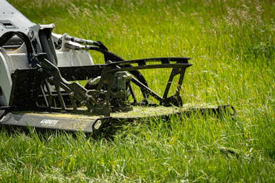 White and black lawn mower cutting green grass in a field