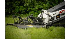 Bobcat skid steer loader with rotary mower attachment cutting grass in a lawn with green foliage background