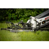 Bobcat skid steer loader with rotary mower attachment cutting grass in a lawn with green foliage background