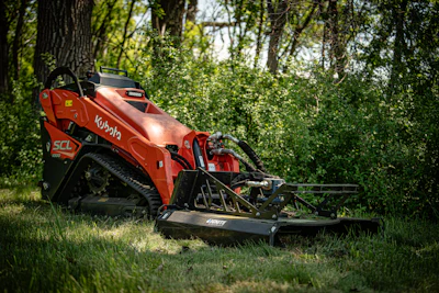 Red Kubota SCL combine harvester with header attachment parked in grassy field with trees