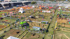 Aerial view of large agricultural equipment exhibition with machinery displays, vendor tents, and crowds at outdoor fairground.
