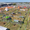 Aerial view of large agricultural equipment exhibition with machinery displays, vendor tents, and crowds at outdoor fairground.
