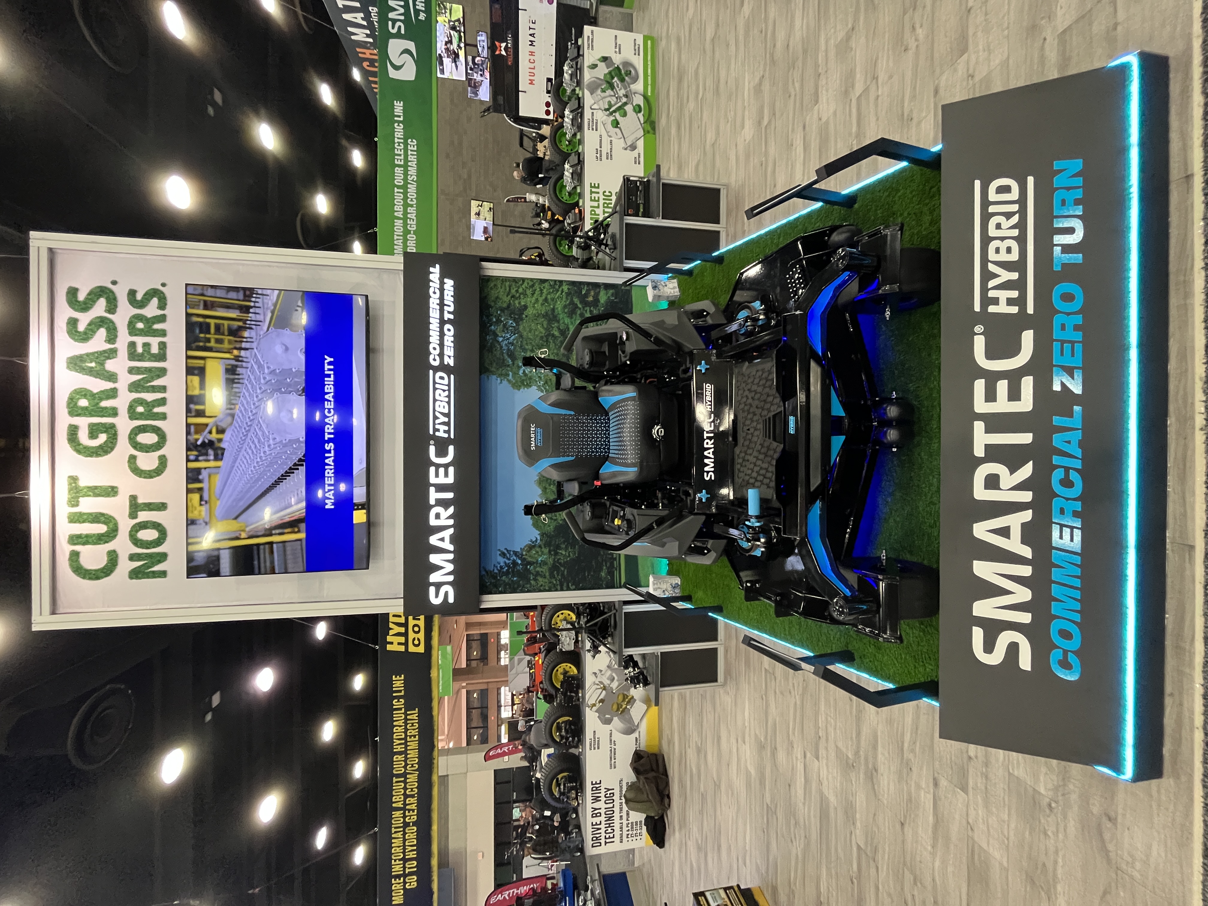 SMARTEC Hybrid Commercial Zero Turn mower displayed at trade show booth with green artificial grass and branded signage