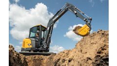 Yellow and black John Deere excavator digging earth at a construction site under blue sky