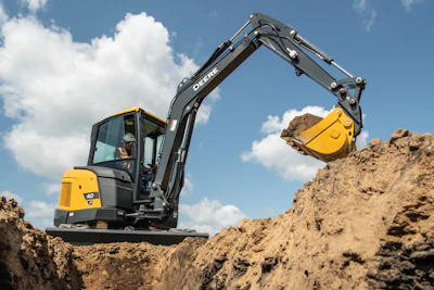 Yellow and black John Deere excavator digging earth at a construction site under blue sky