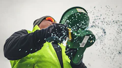 Worker in safety gear holding green buckets with water splashing against white background