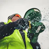 Worker in safety gear holding green buckets with water splashing against white background