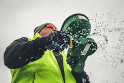 Worker in safety gear holding green buckets with water splashing against white background