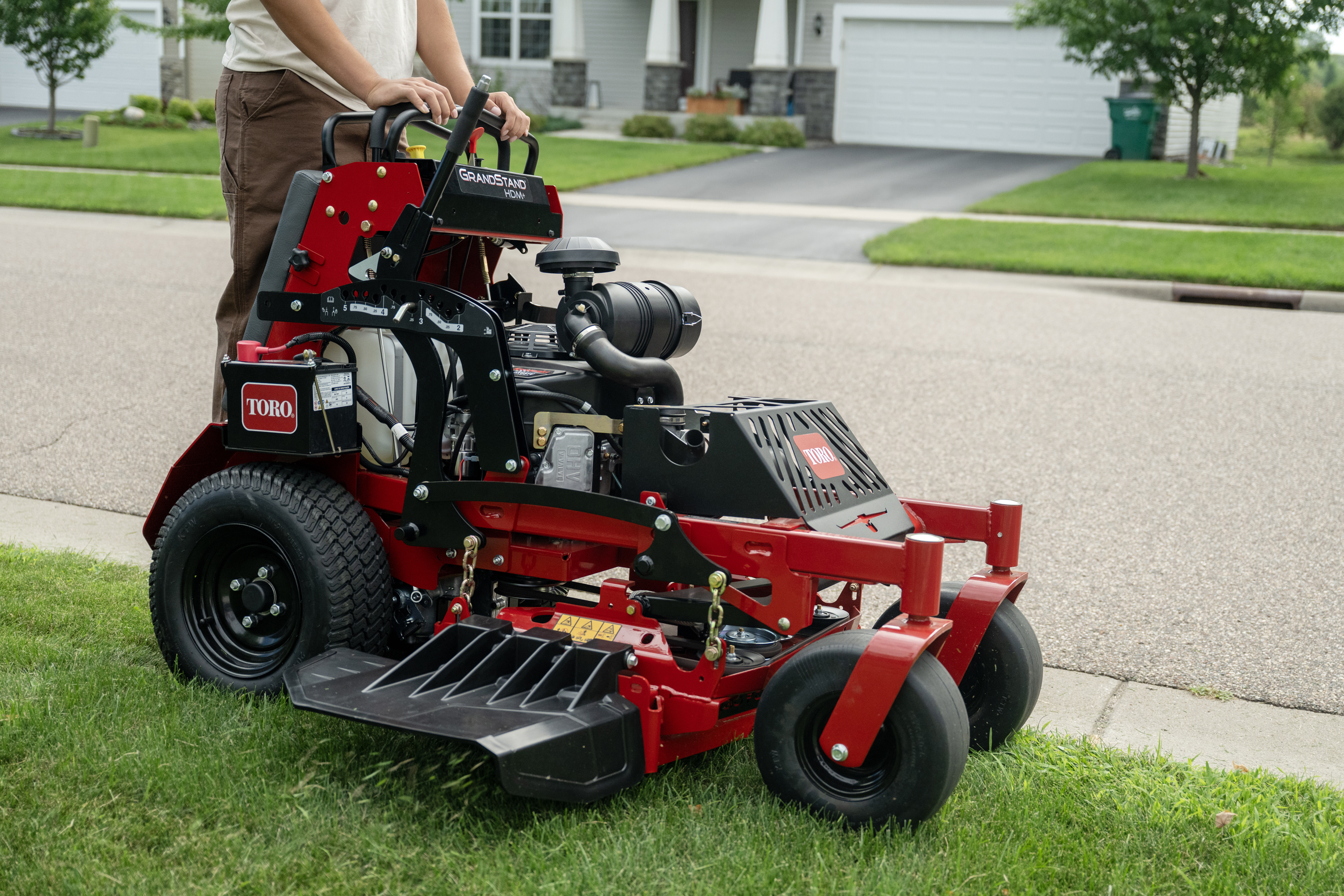 Red and black Toro zero-turn radius mower on residential driveway with operator