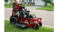 Red and black Toro zero-turn radius mower on residential driveway with operator