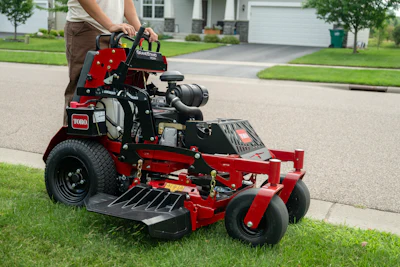 Red and black Toro zero-turn radius mower on residential driveway with operator
