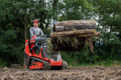 Worker operating red wood chipping machine with large logs in outdoor forest setting