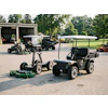 Landscaping equipment including zero-turn mowers and utility vehicles displayed in a commercial yard with storage building