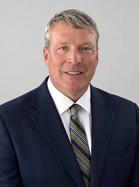 Professional headshot of a middle-aged man in navy blazer and striped tie smiling at camera
