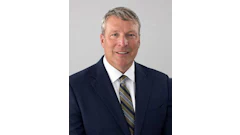 Professional headshot of a middle-aged man in navy blazer and striped tie smiling at camera